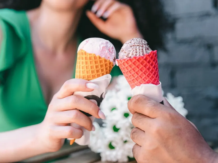 Four hands holding up pastel green, orange, pink and blue cones against a yellow wall