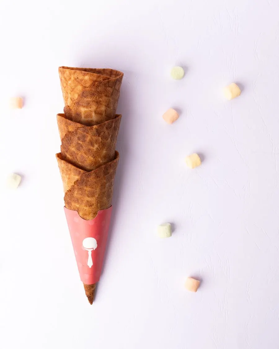 Three empty waffle cones stacked into one pink paper wrap on a pale ground