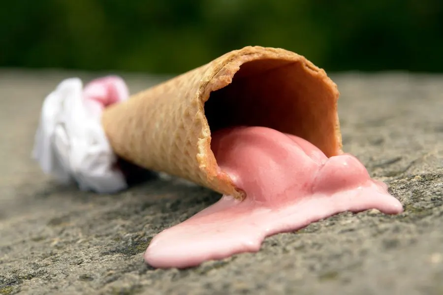 A dropped strawberry cone melting on a stone kerb with grass out of focus behind it