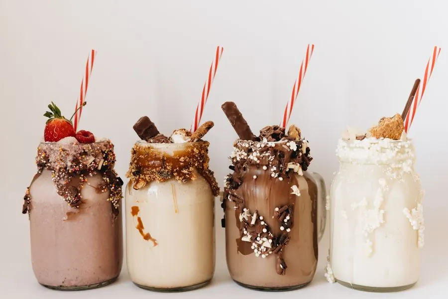 Four loaded milkshakes in glass jars with striped paper straws, side by side