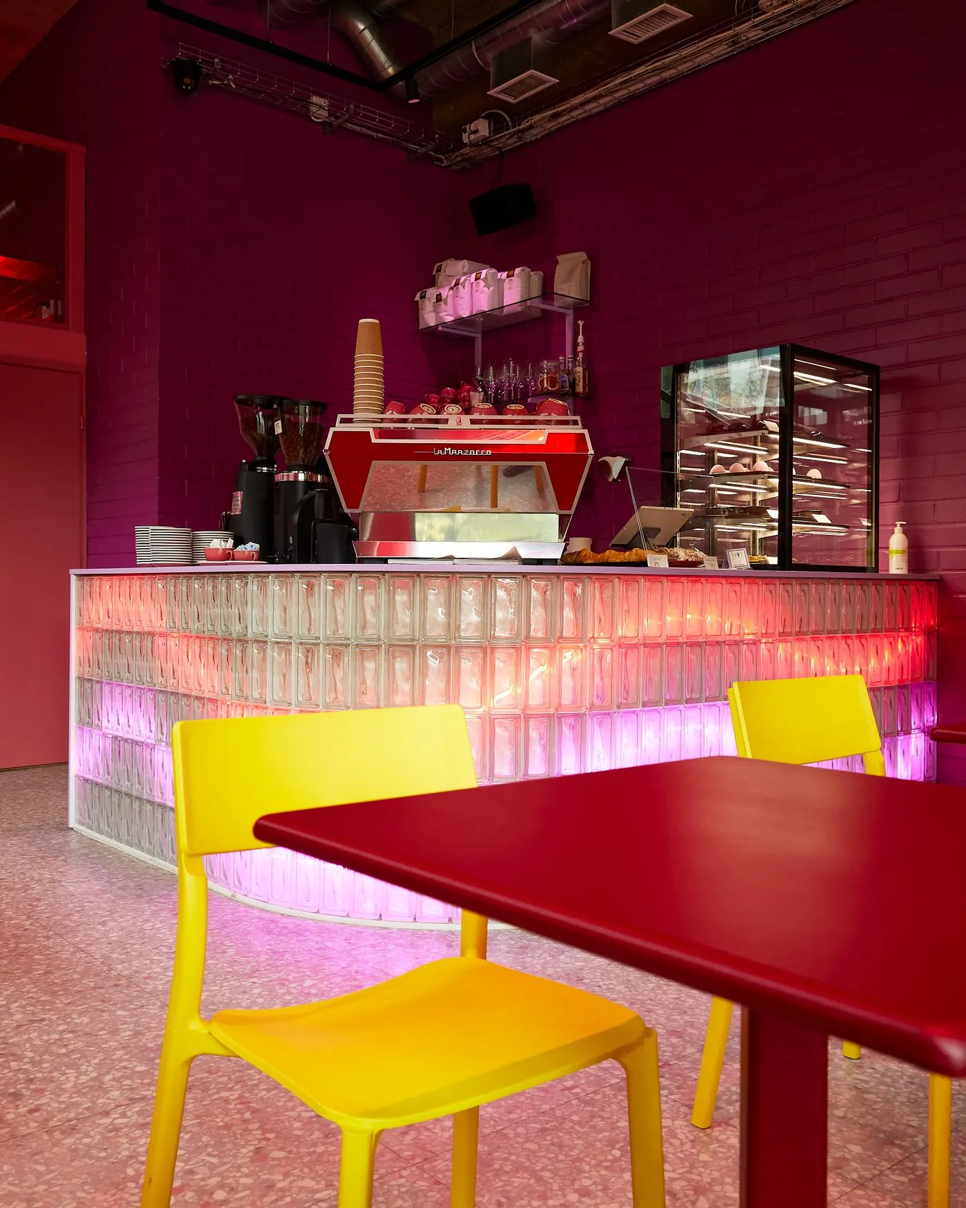 The Osu counter, glass blocks lit pink under a red espresso machine, yellow chairs at a red table
