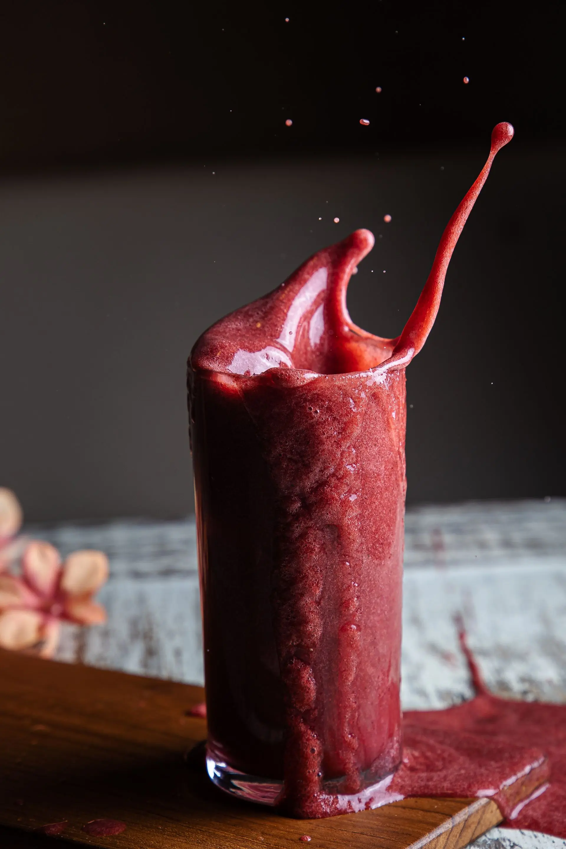 A berry red smoothie erupting in a splash against a dark maroon ground
