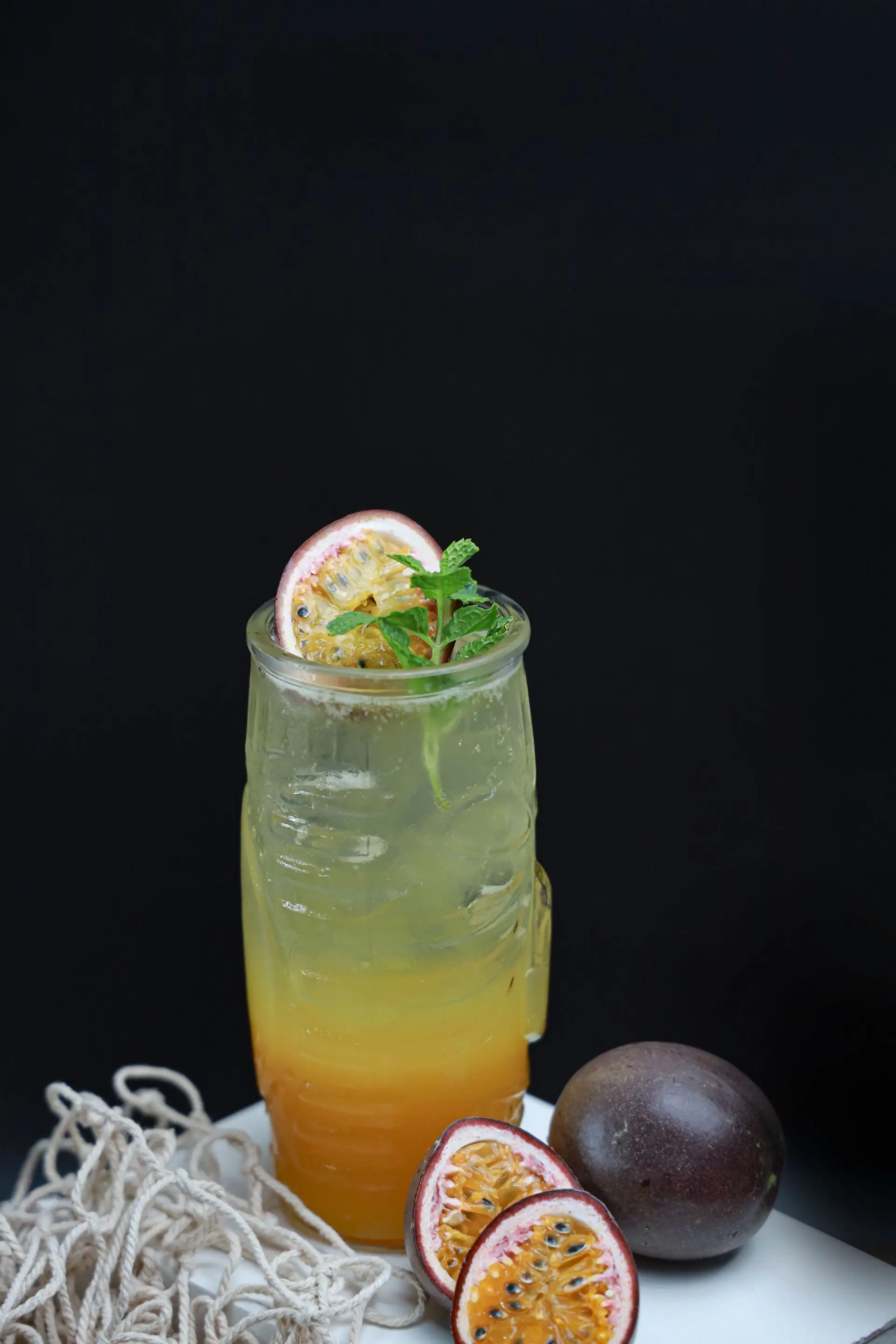 A glass of golden passion fruit drink with a halved passion fruit resting on top