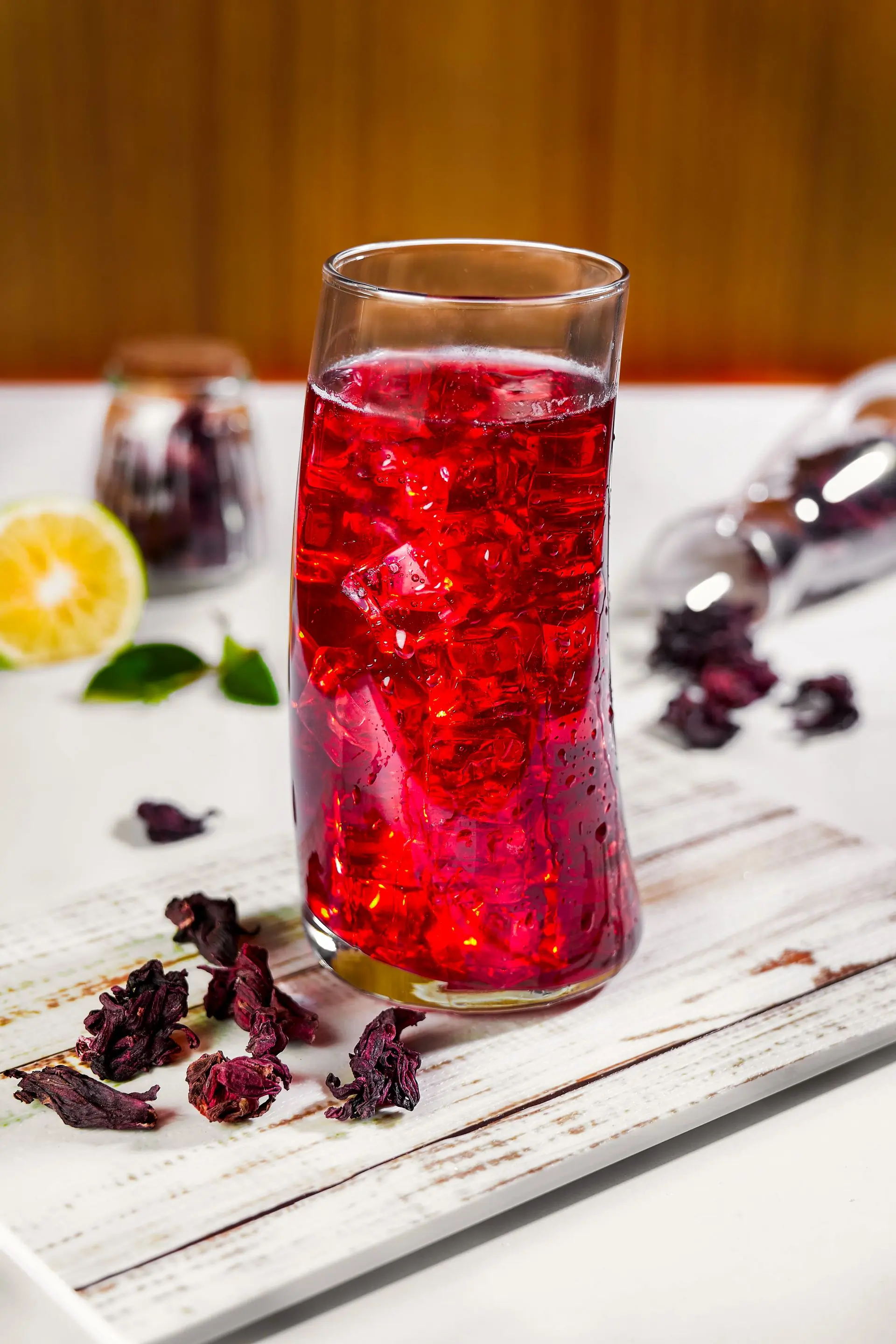 A glass of deep red hibiscus sobolo over ice with a sprig of mint