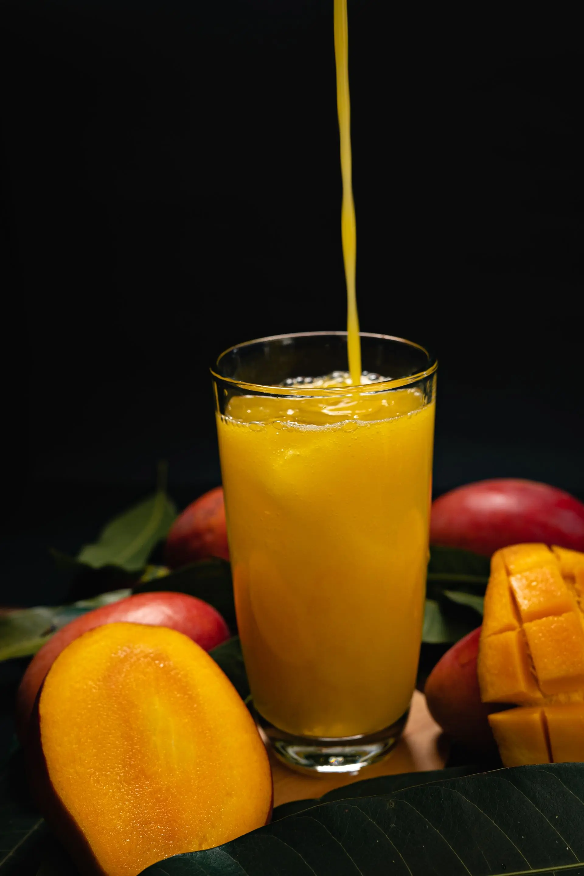 A stream of mango juice pouring into an iced glass on a dark ground