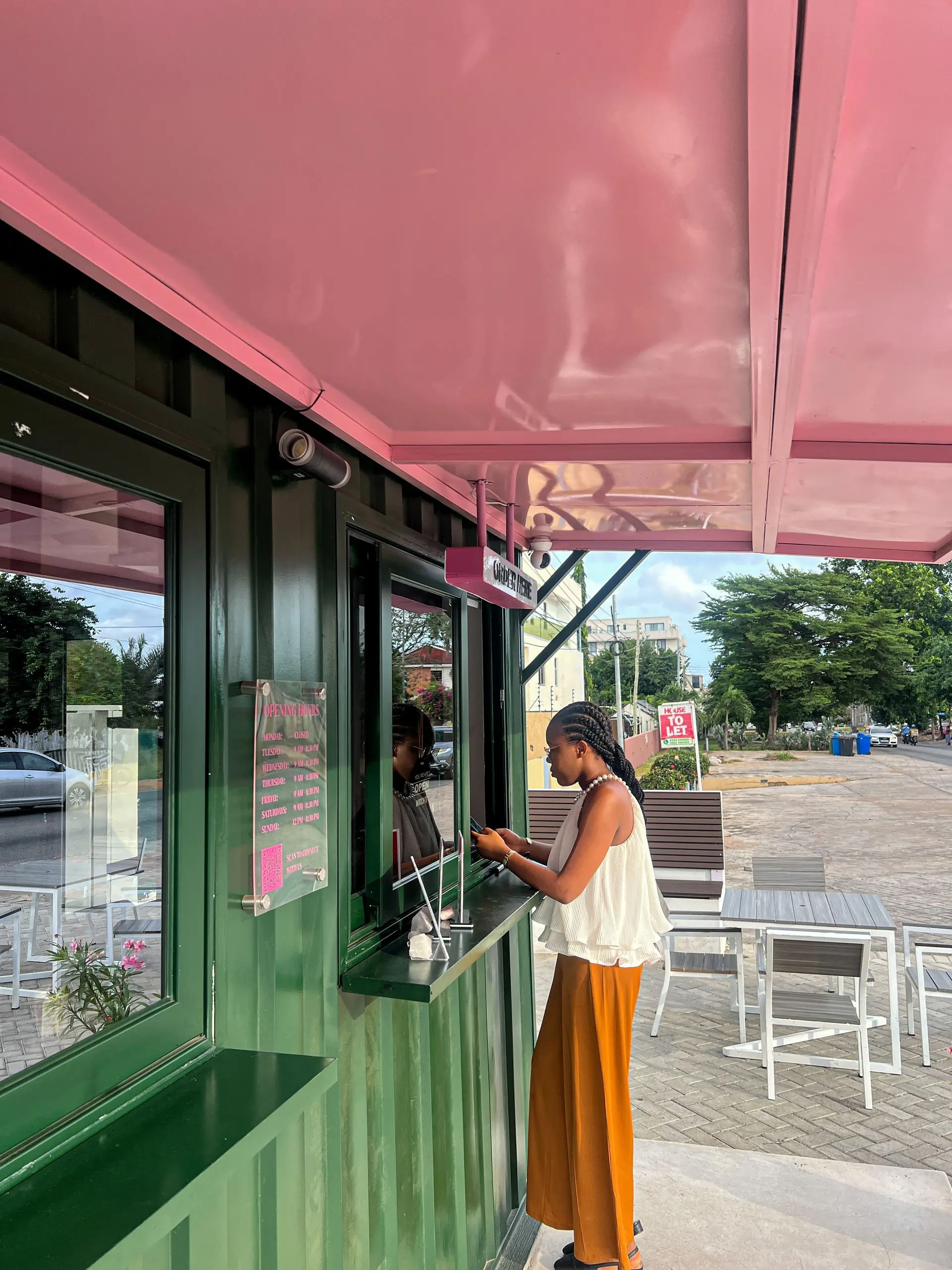 A forest green kiosk with a pink awning and a customer waiting at the window