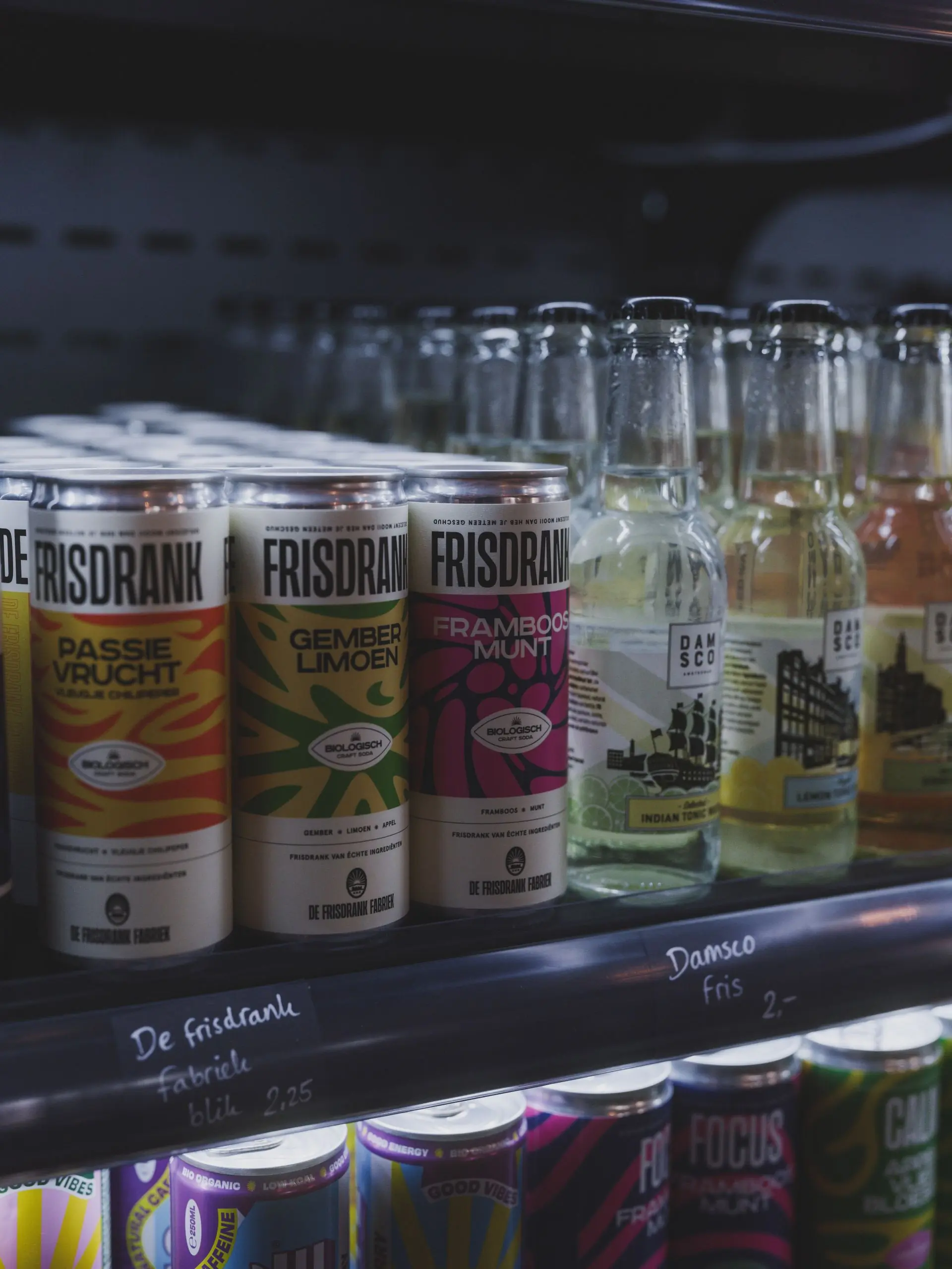 Rows of pastel coloured soda cans chilling on the shelf of a dark fridge