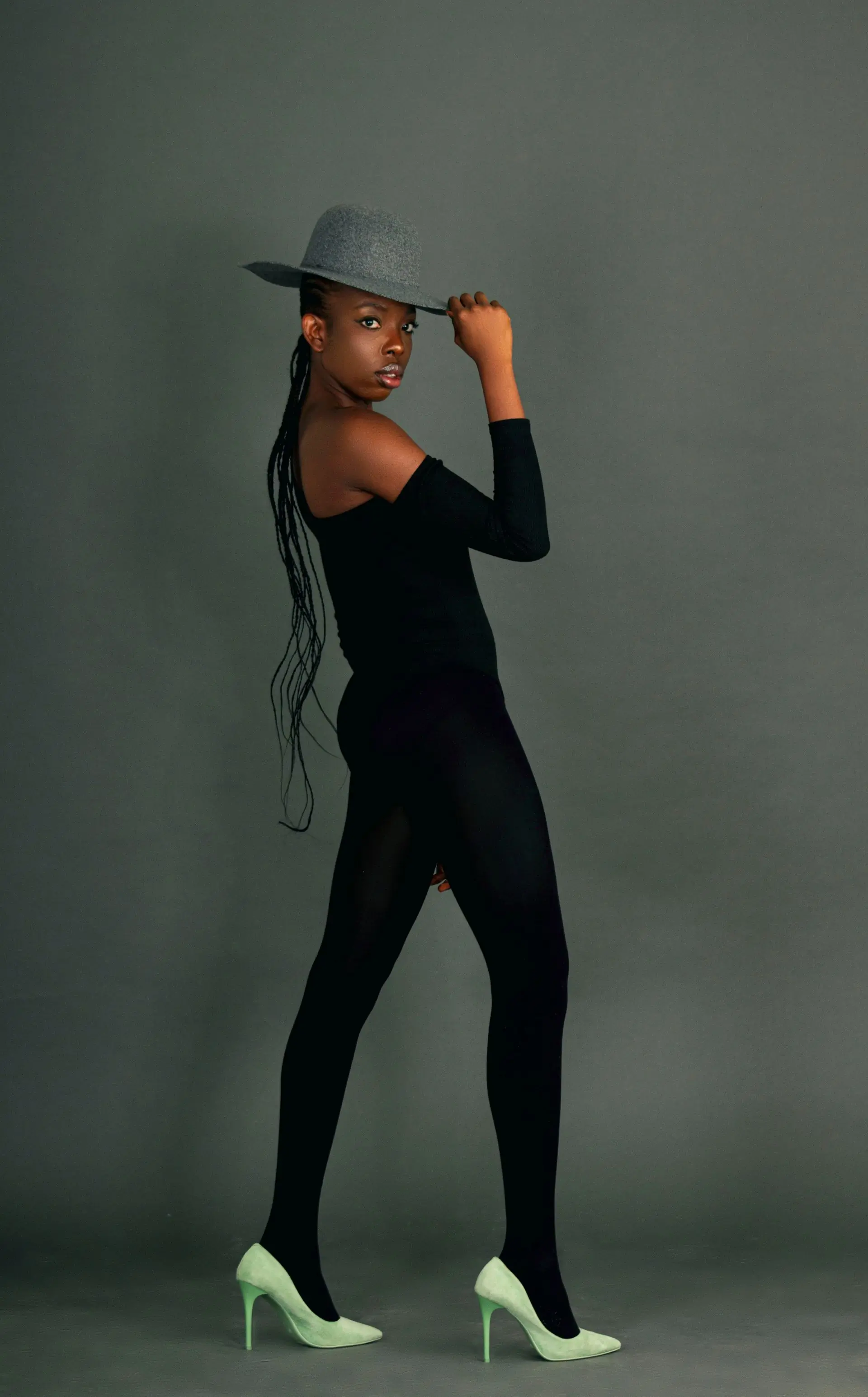 A model in a black knit and a felt hat against a plain studio wall