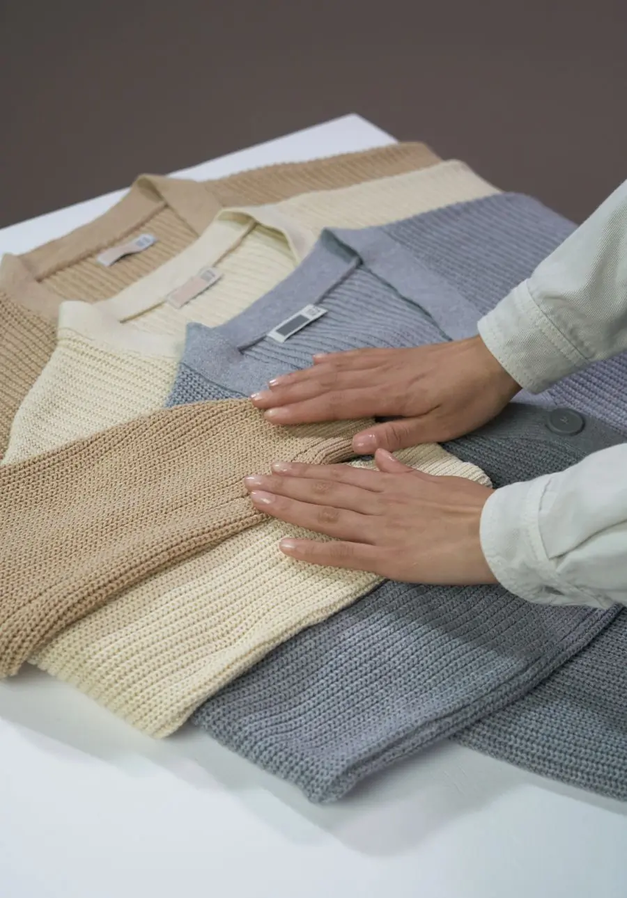 Hands smoothing a folded knit jumper on a table