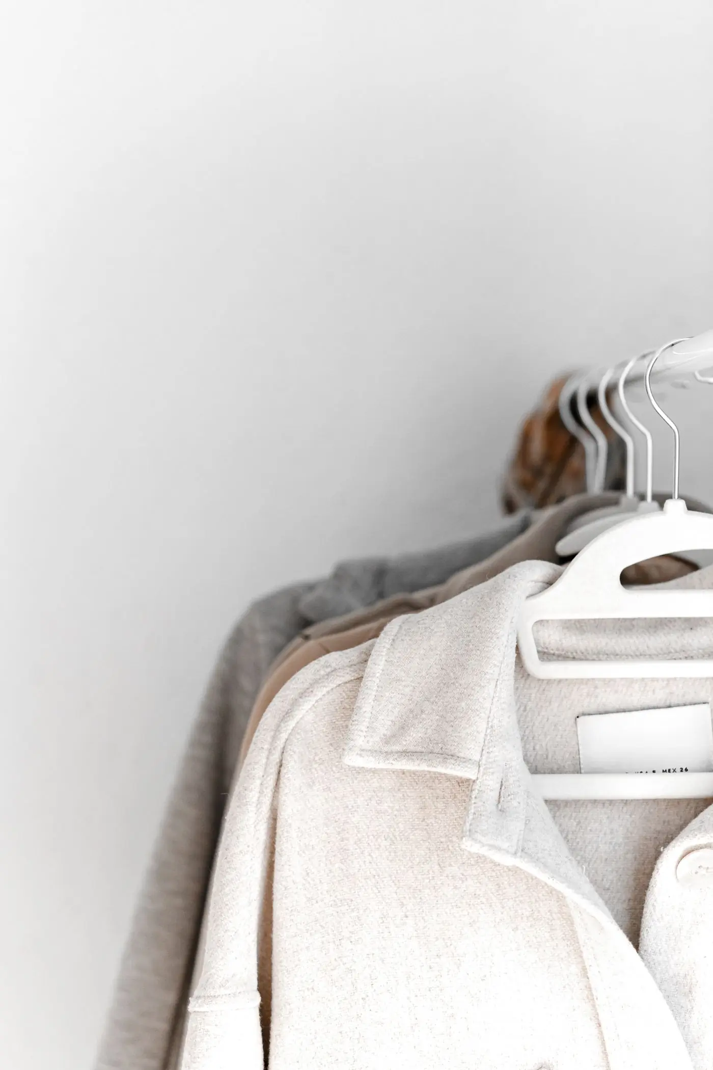 Neutral-coloured clothes hanging close together on white hangers