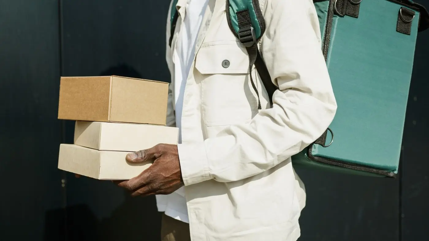 A courier carrying two boxes along a street