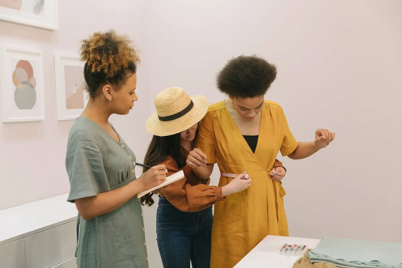 Three people fitting a dress on a stand and marking the length