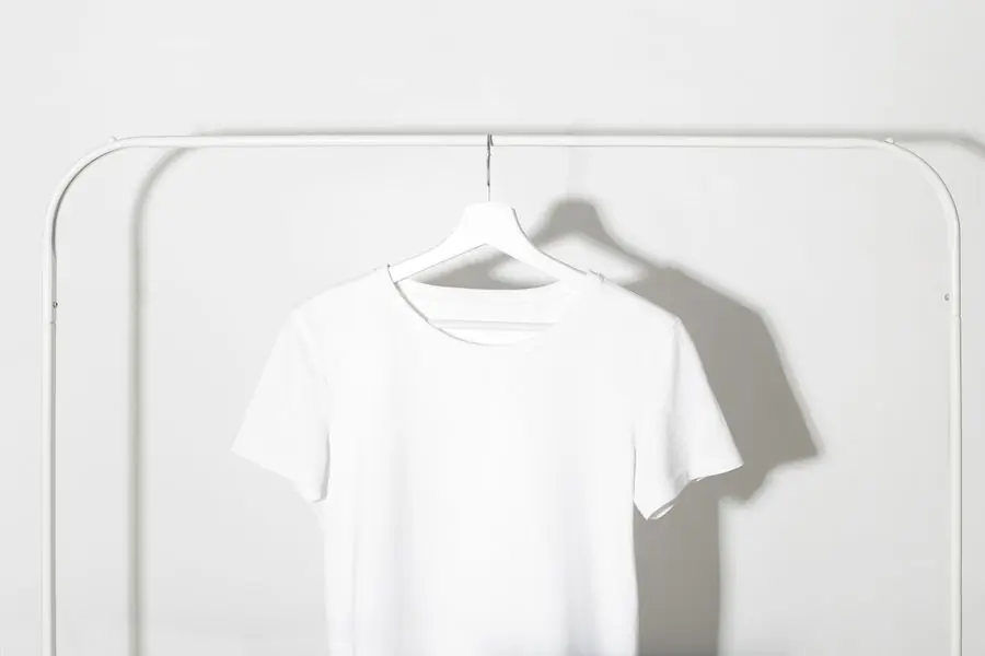 A plain white cotton t-shirt on a hanger against a pale wall