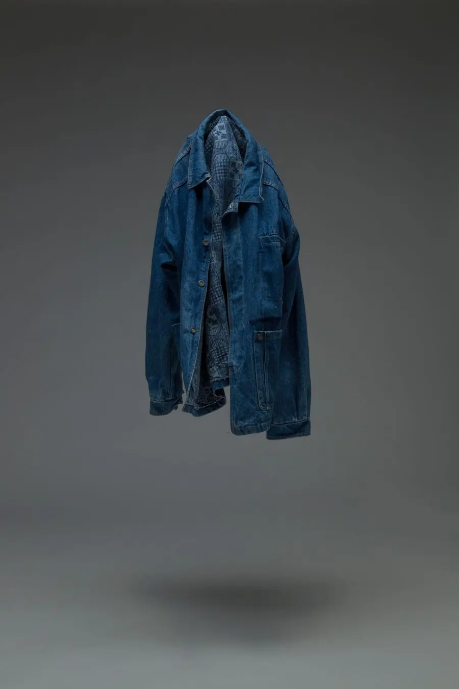 An indigo denim jacket suspended against a grey ground