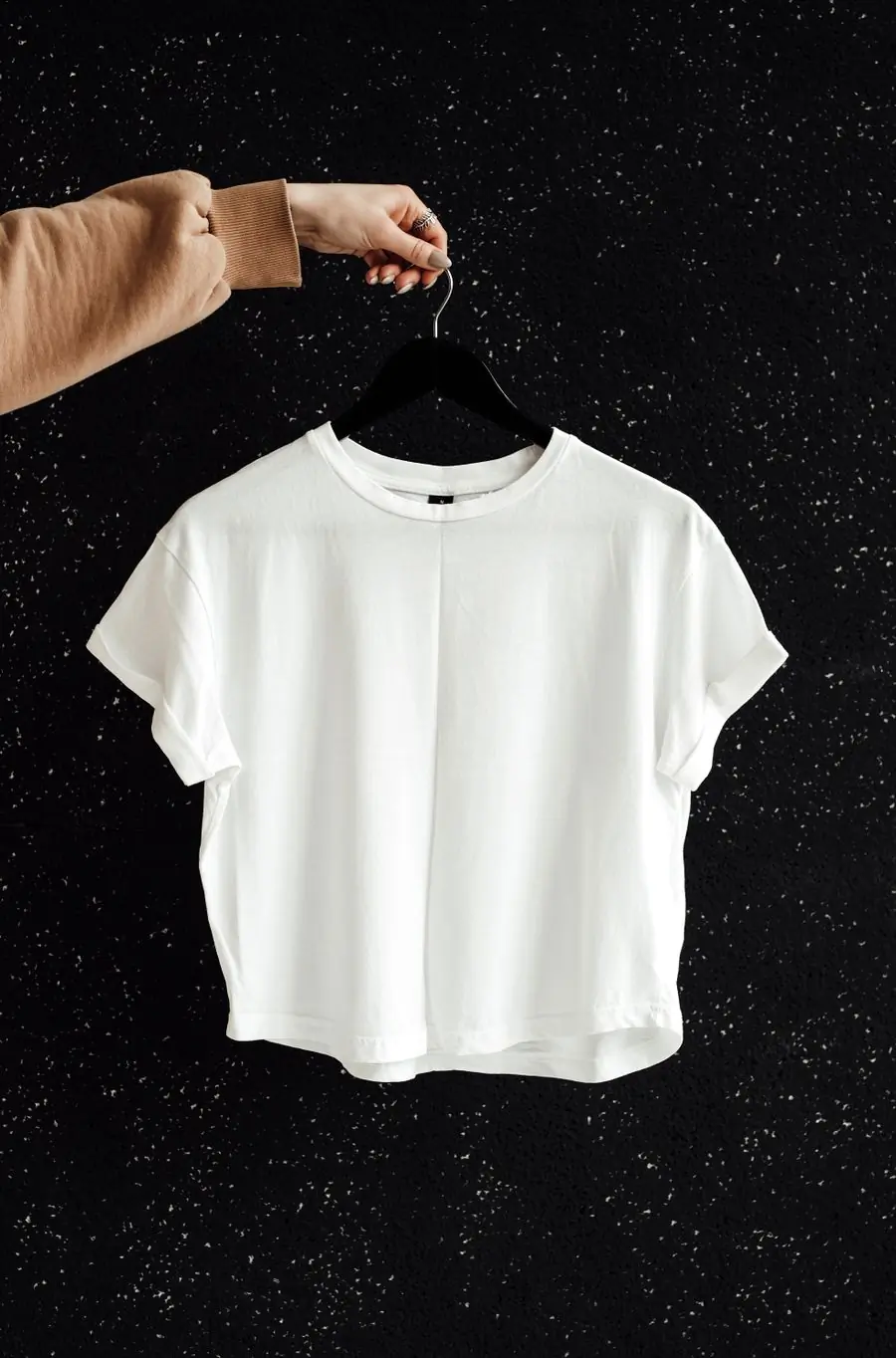 A white heavyweight t-shirt on a hanger against a dark speckled wall
