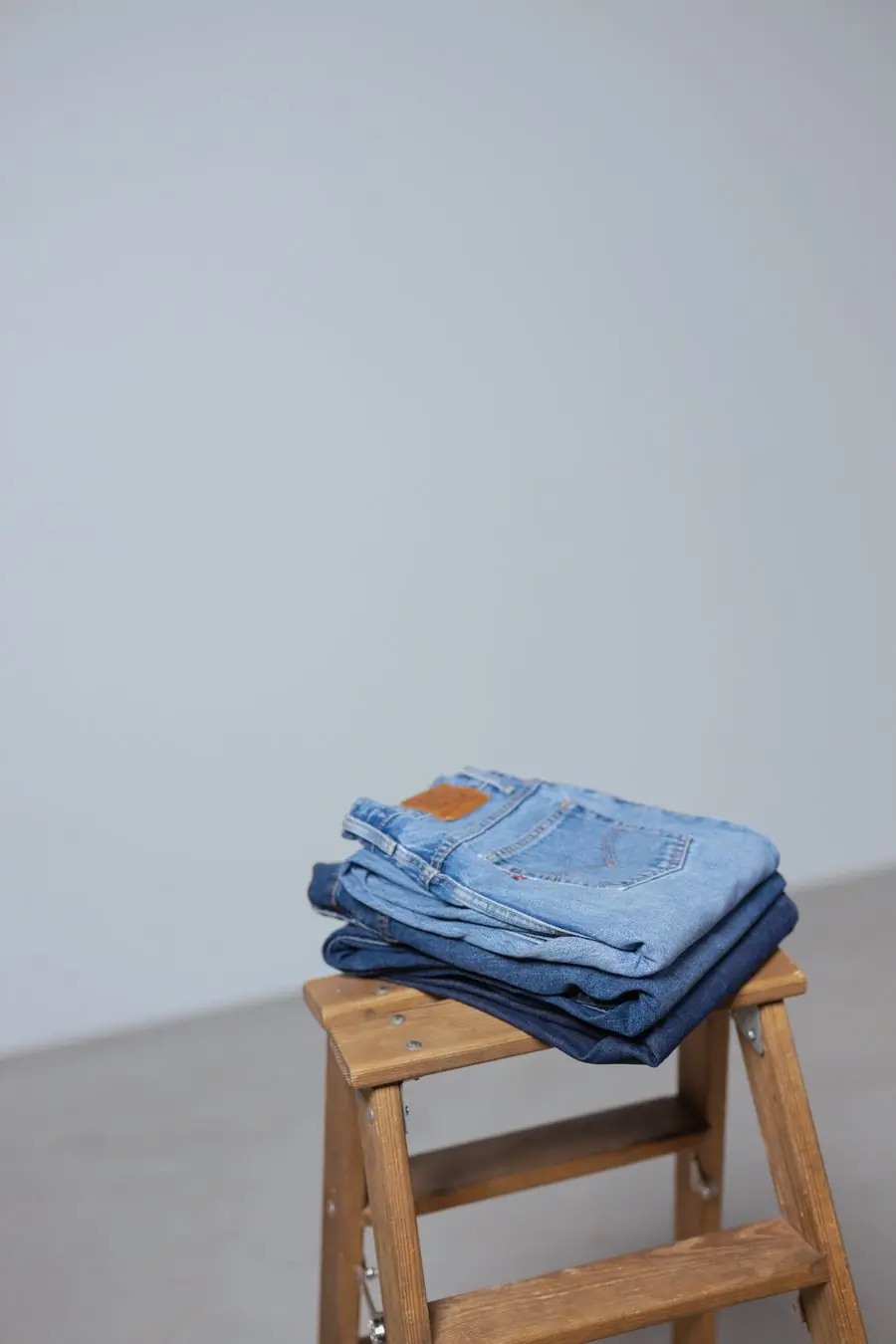 Folded straight-leg jeans stacked on a wooden stool