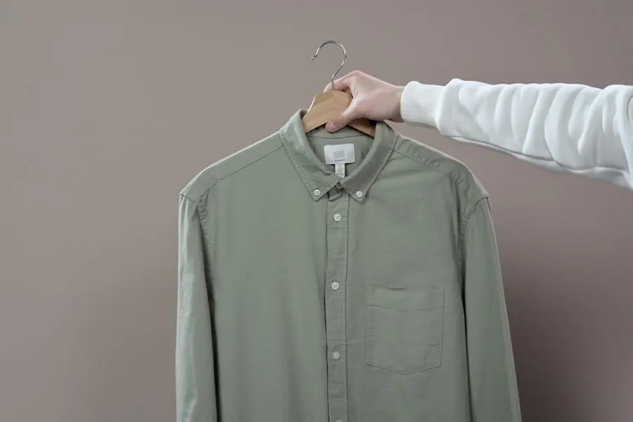 A sage-green poplin shirt held out on a hanger