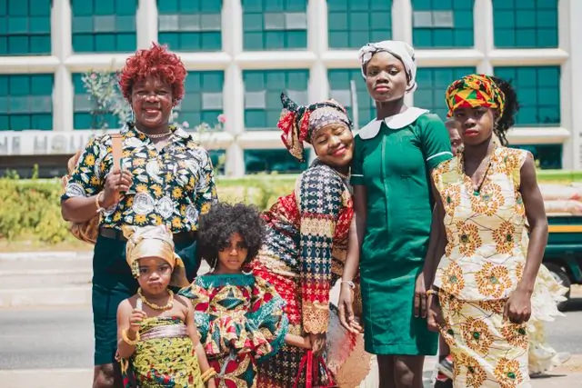 A group in bright printed dresses outside a tall building