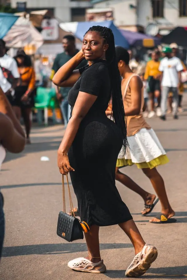 A cropped shot of a black dress and a woven bag on the street