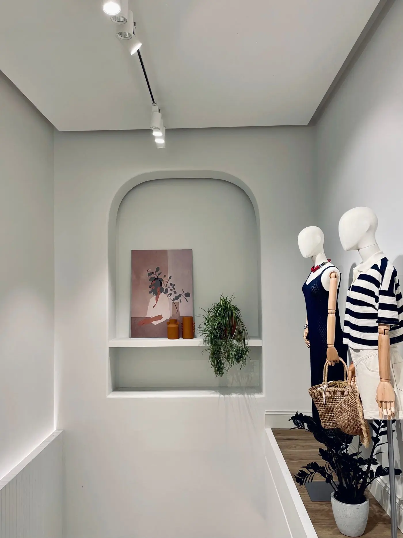Two mannequins beside an alcove of ceramics and plants