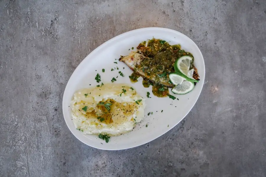 A white plate of fish with lemon and olive oil
