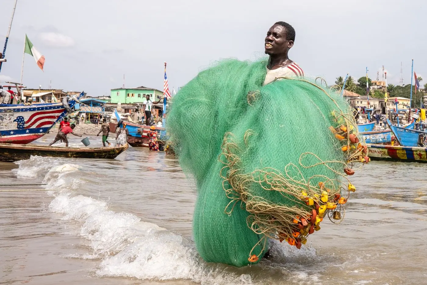 A fisherman carrying green nets at Elmina harbour