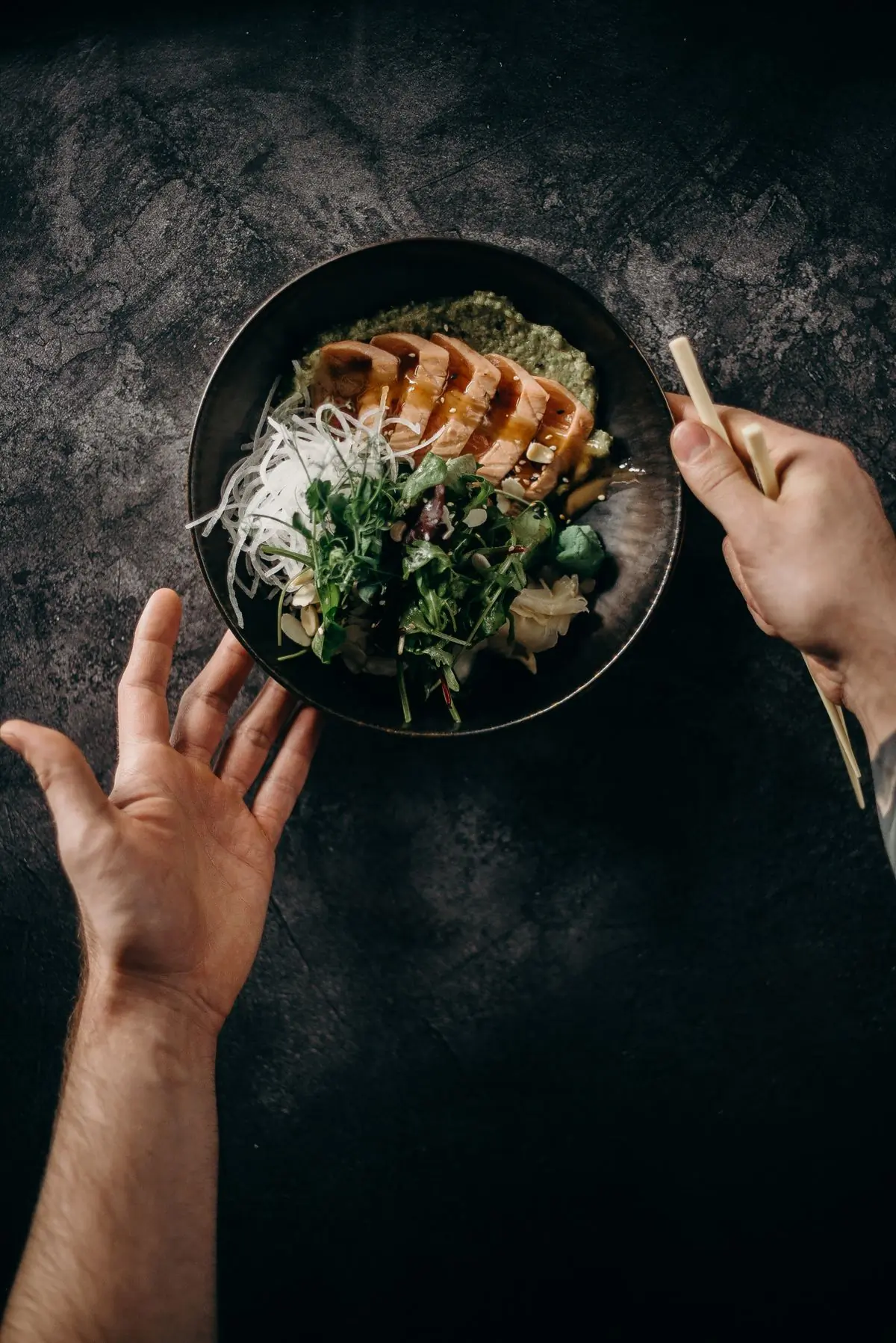 A black ceramic bowl of dressed greens held in two hands
