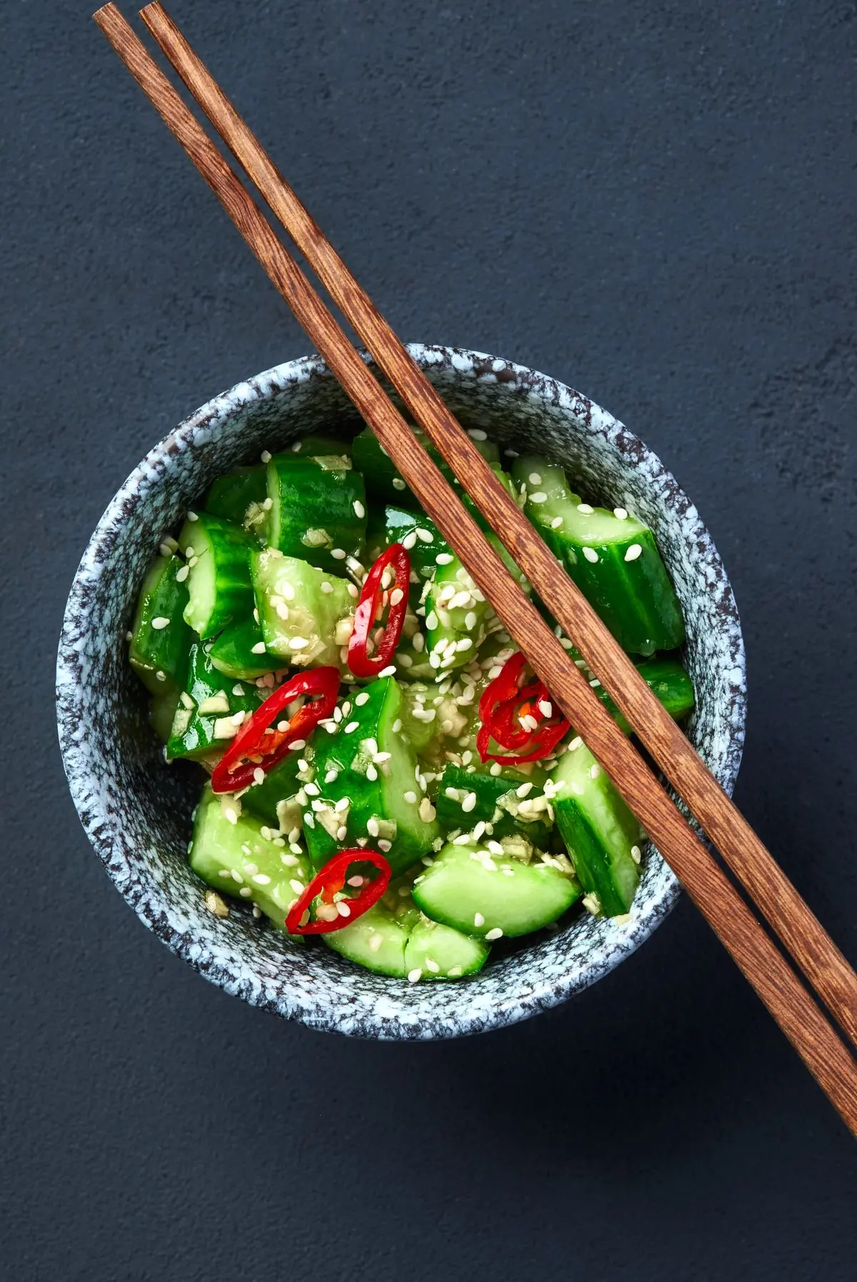 A dark bowl of cucumber salad with chilli and sesame