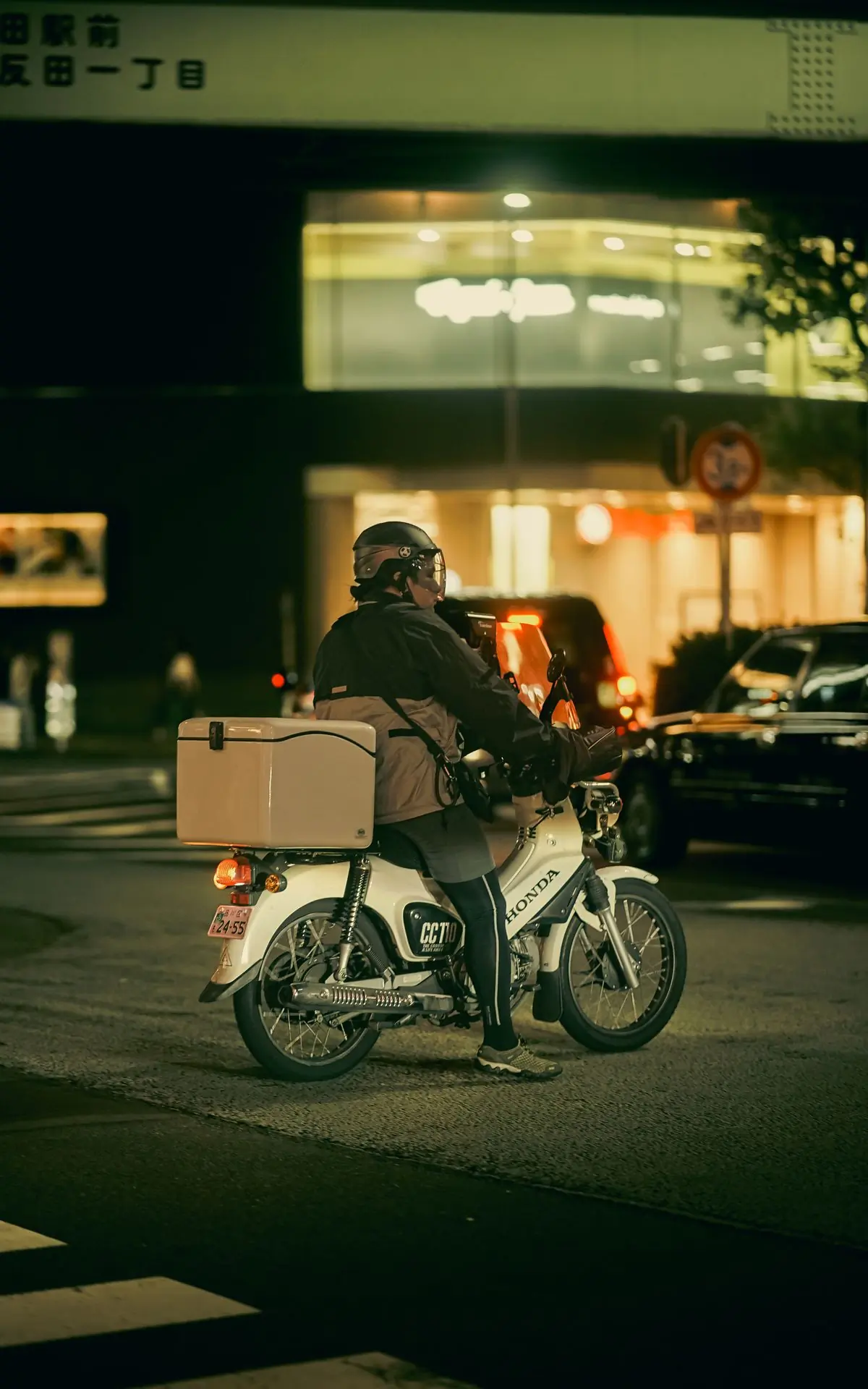 A rider carrying a delivery box through the city at night