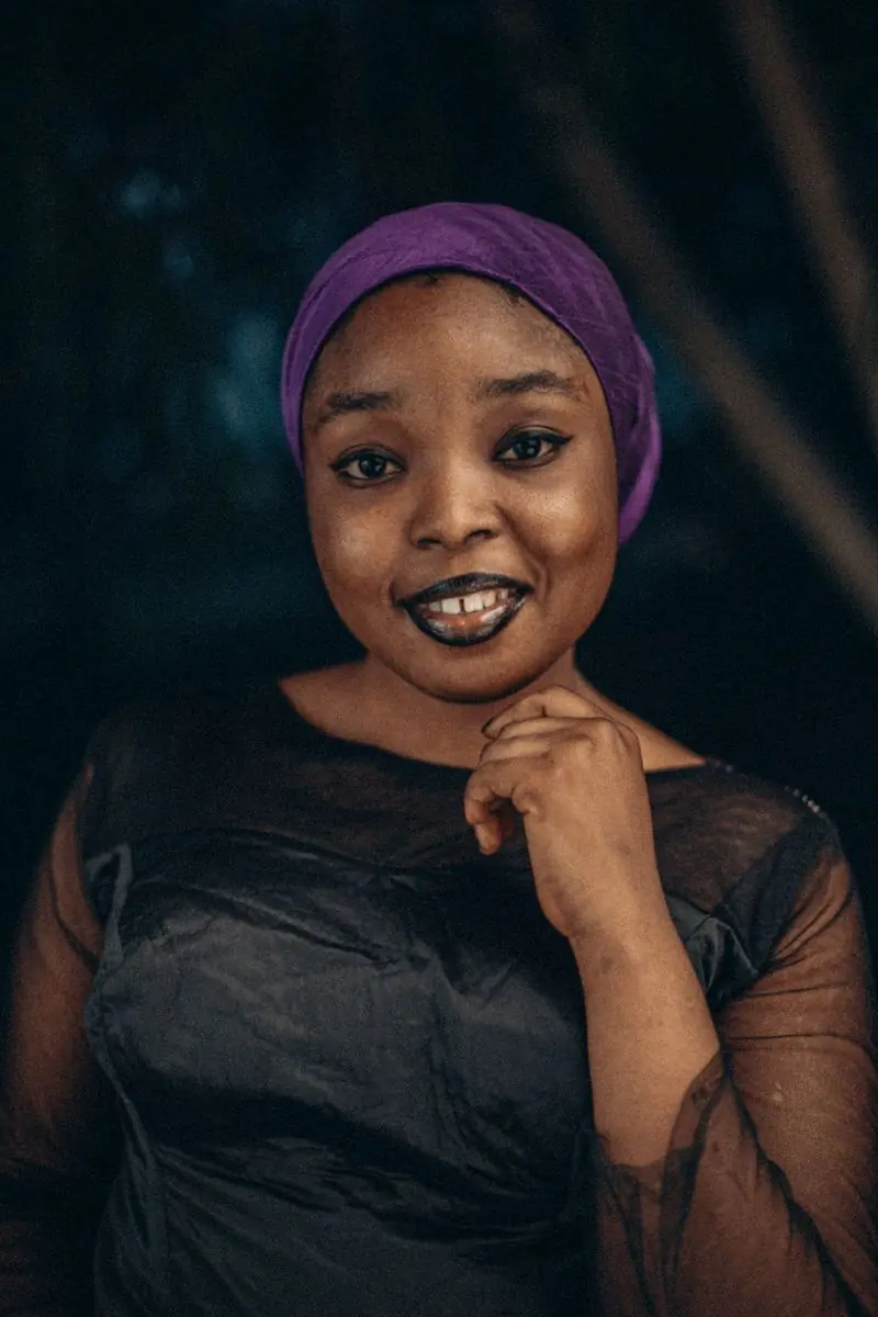 A smiling woman in a purple headwrap against a dark ground