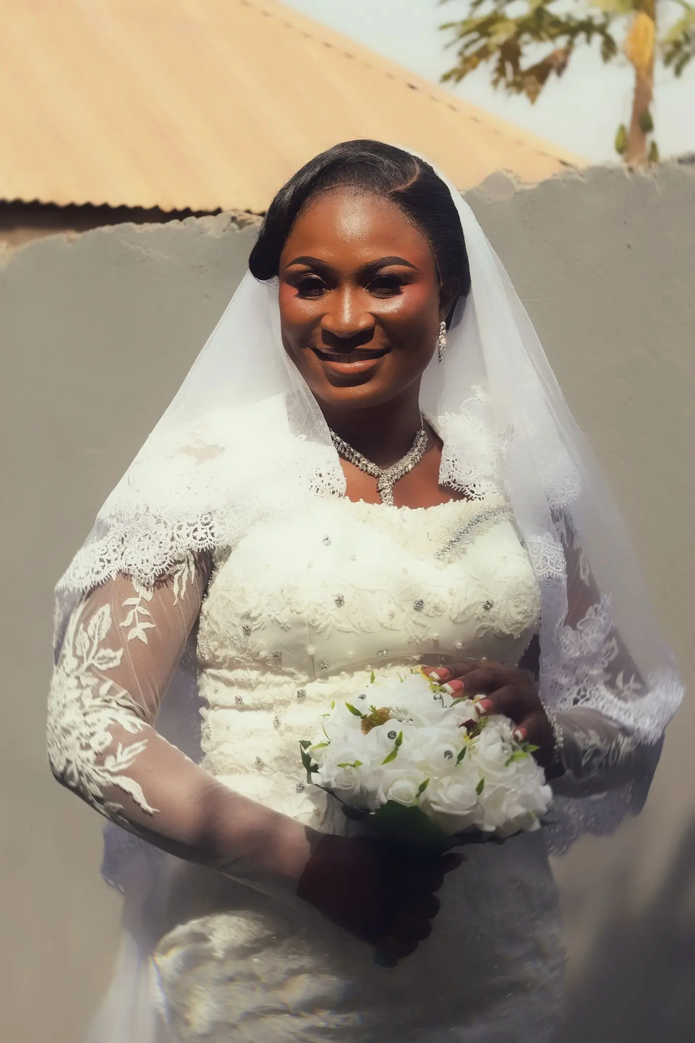 A bride in a white lace gown and veil standing on her own