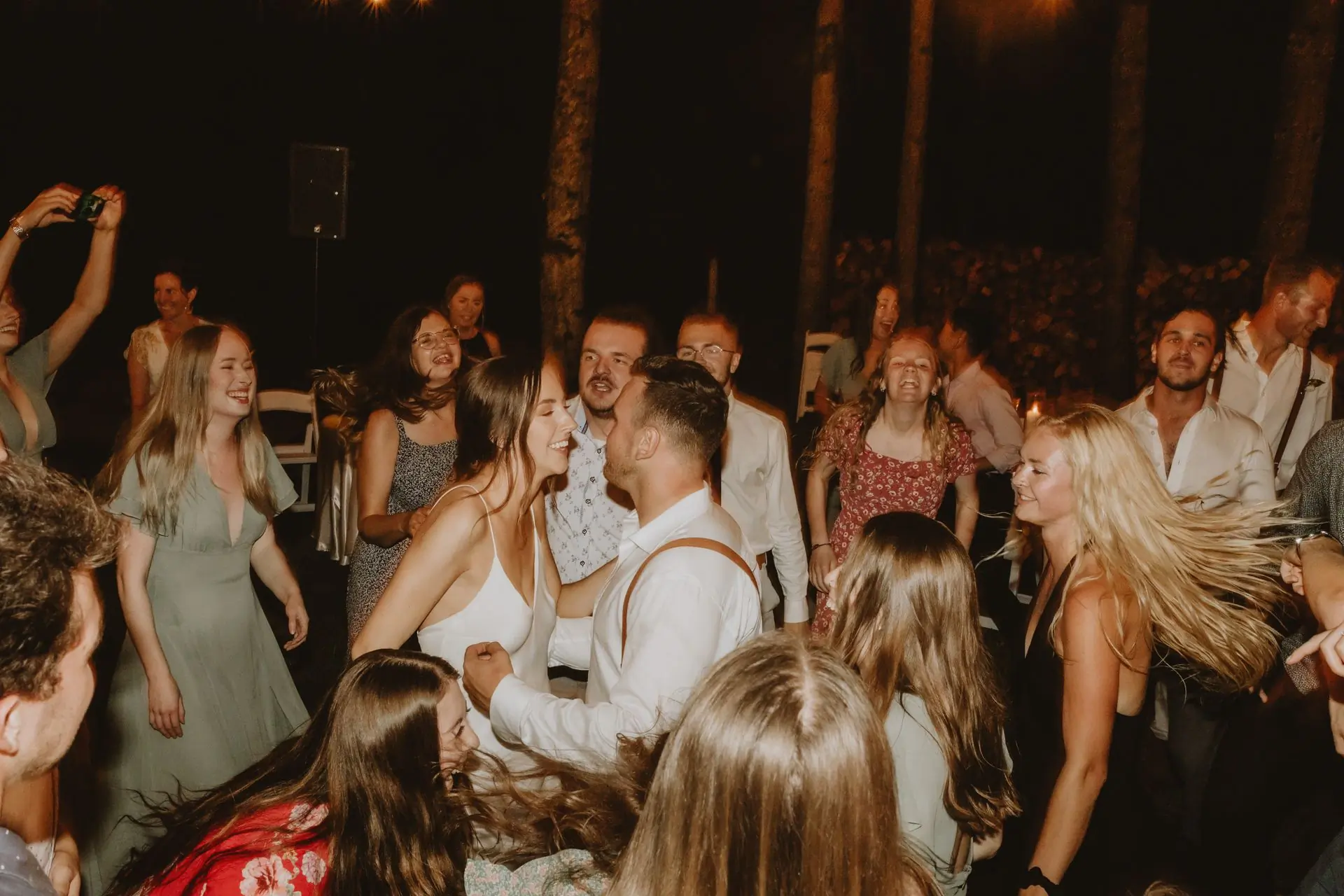 Wedding guests dancing together under warm light at a reception