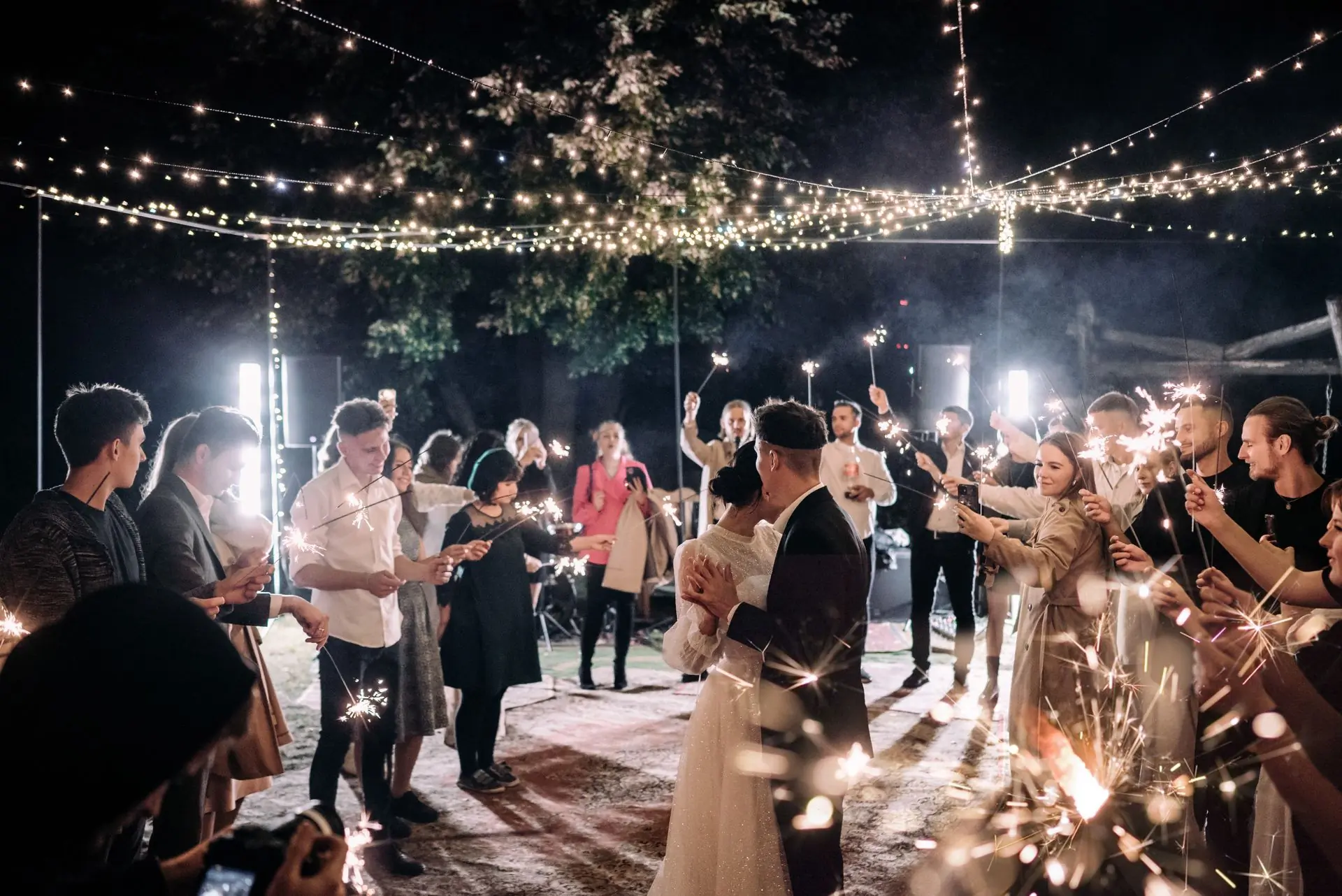 Guests holding sparklers in a circle around a couple dancing at night