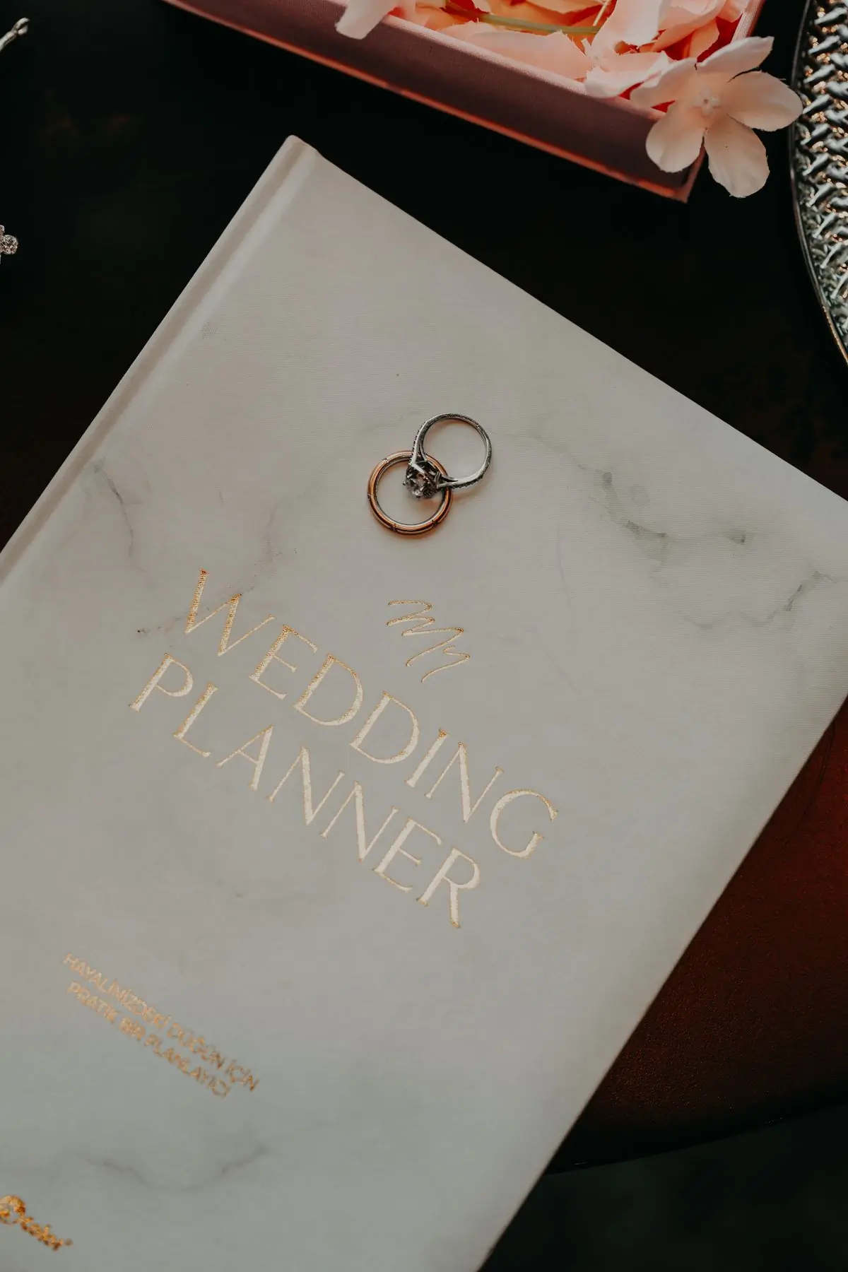 A wedding planner's notebook on a marble table with two gold rings resting on it