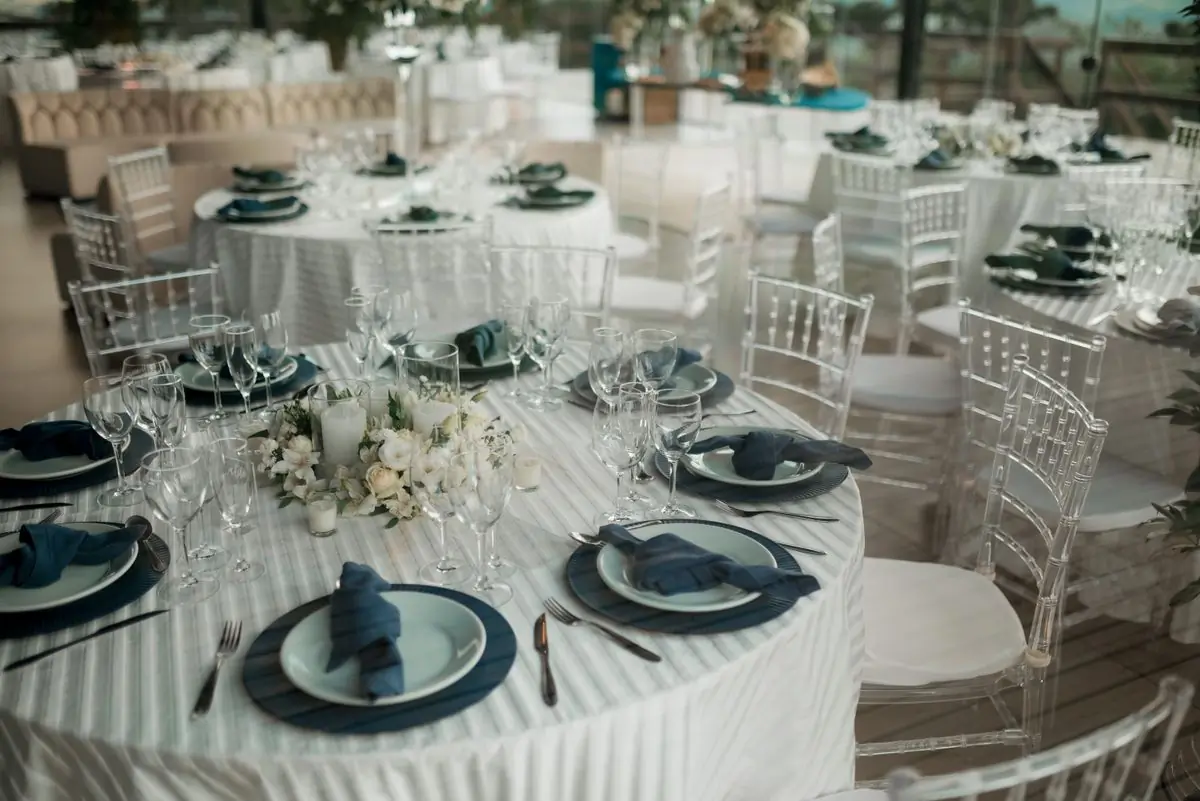 A round reception table laid with dark plates, white linen and low white flowers