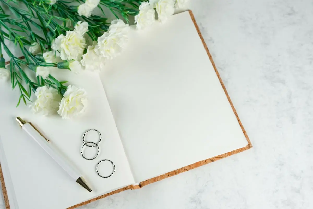 A pair of wedding rings resting on an open notebook beside white flowers