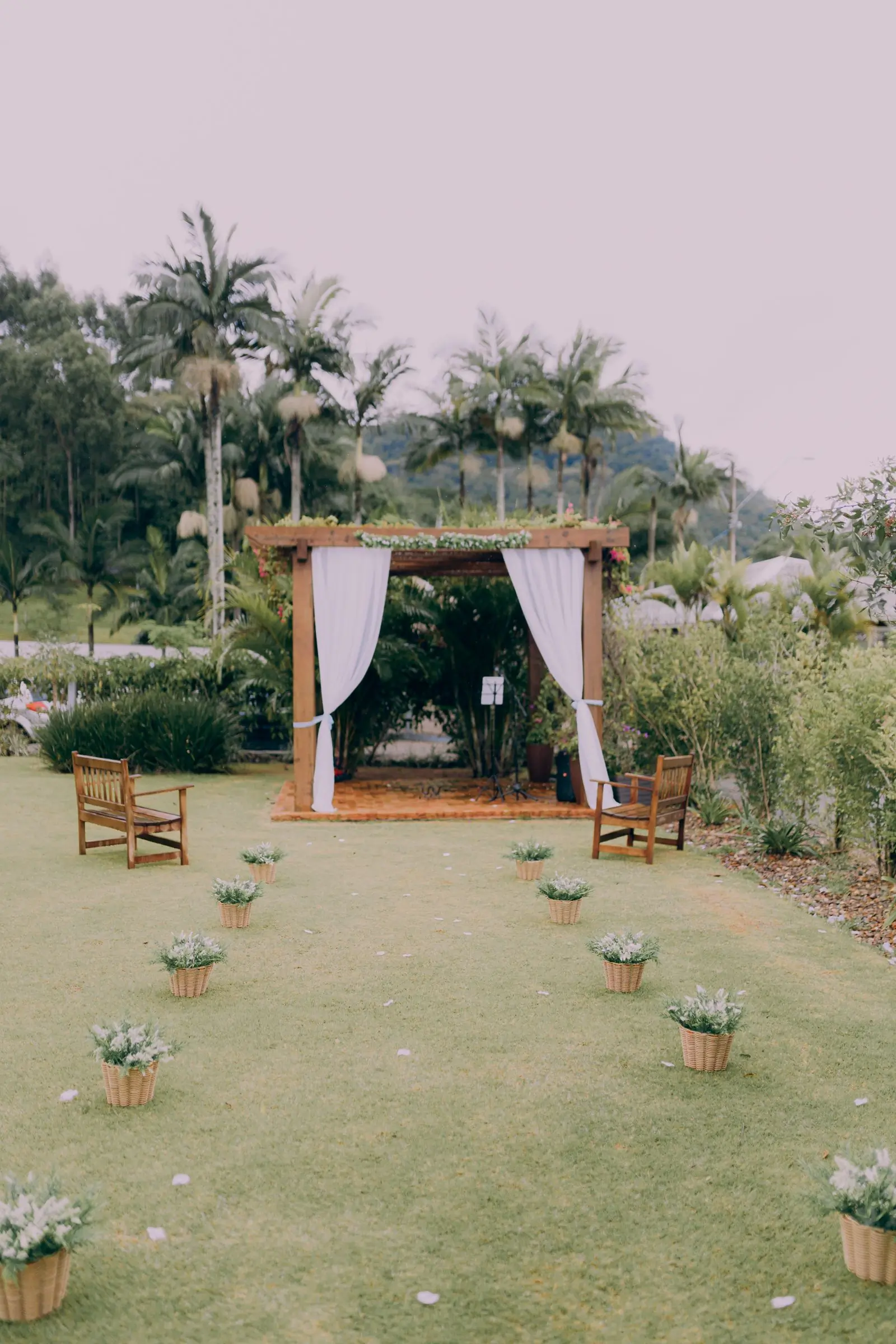 A simple wooden wedding arch draped in white linen in a garden at dusk