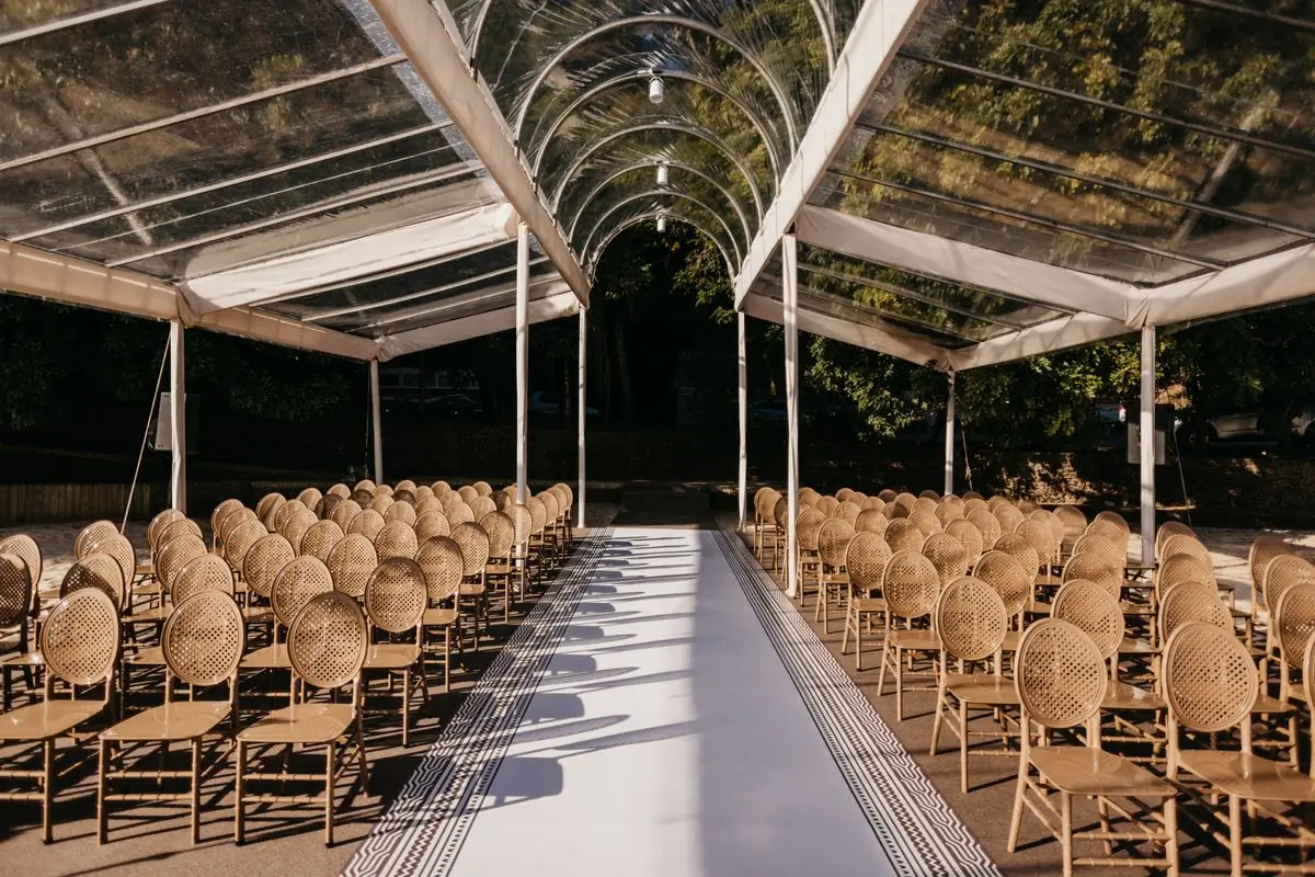 A long aisle of chairs set out under a glass canopy before a ceremony