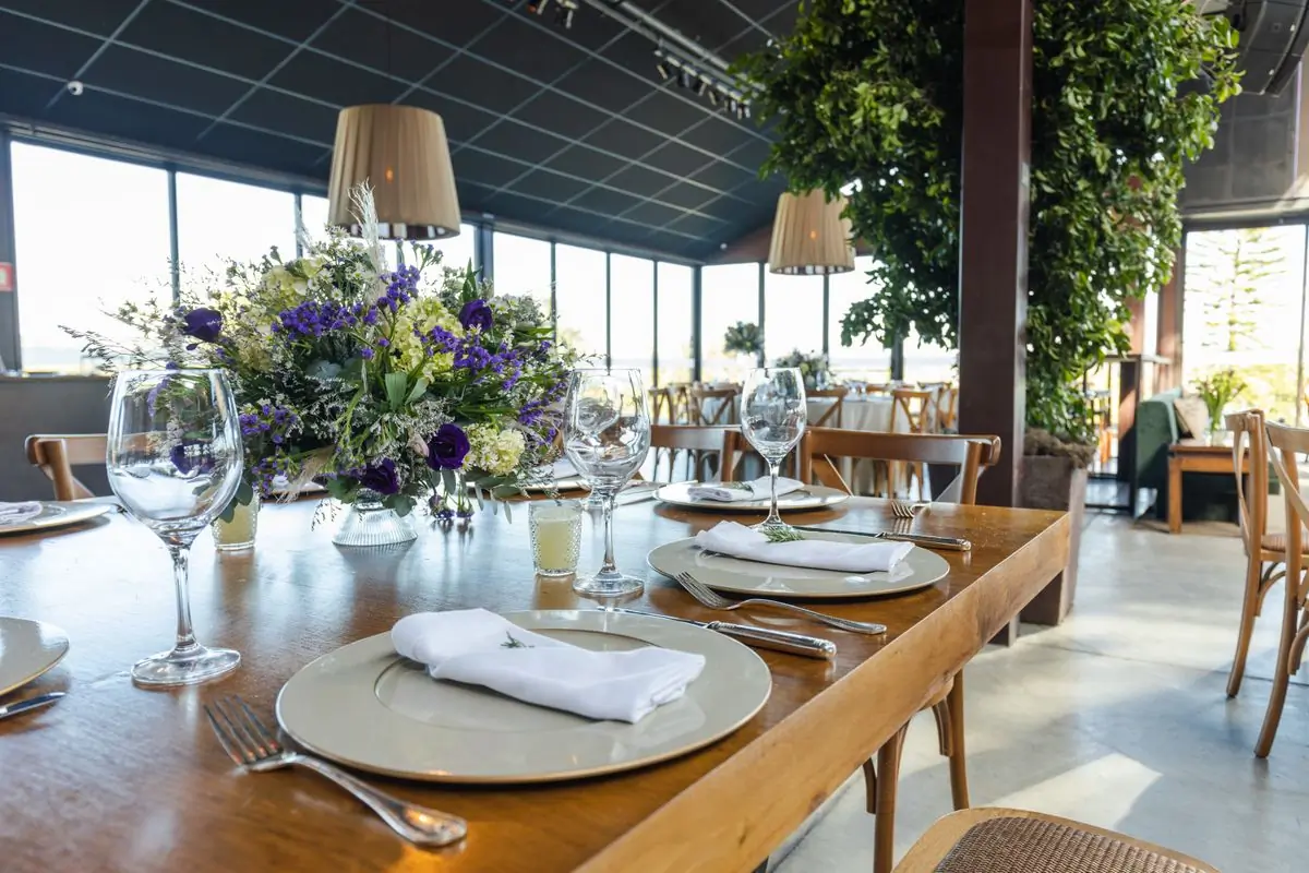 A long table laid for dinner beside a wall of windows looking onto greenery