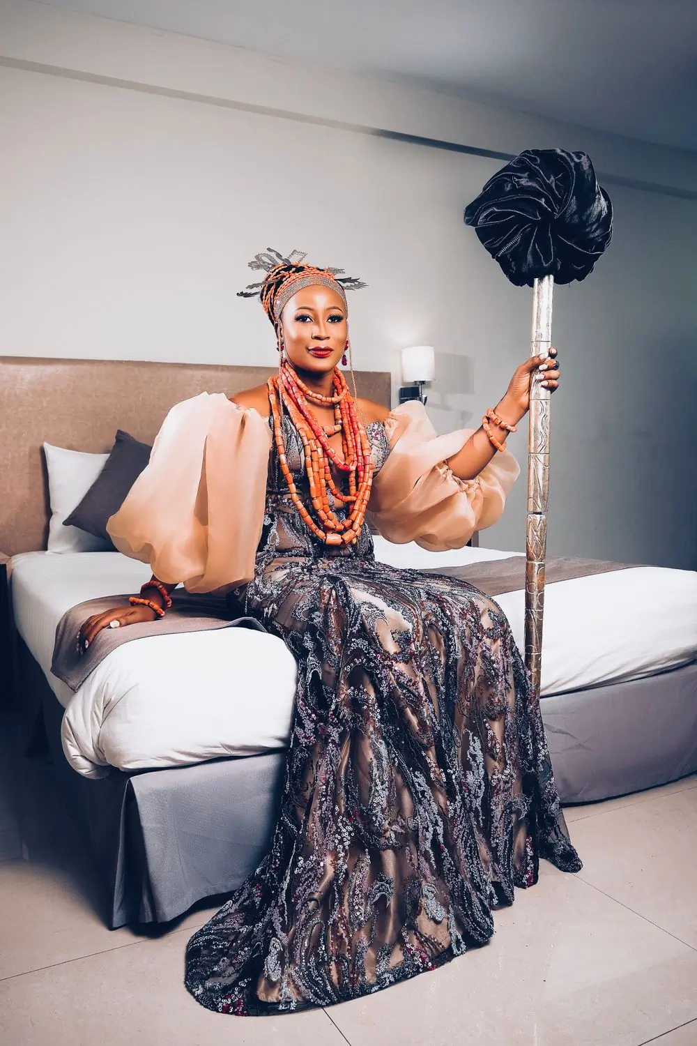 A woman in a patterned gown seated with a ceremonial fan