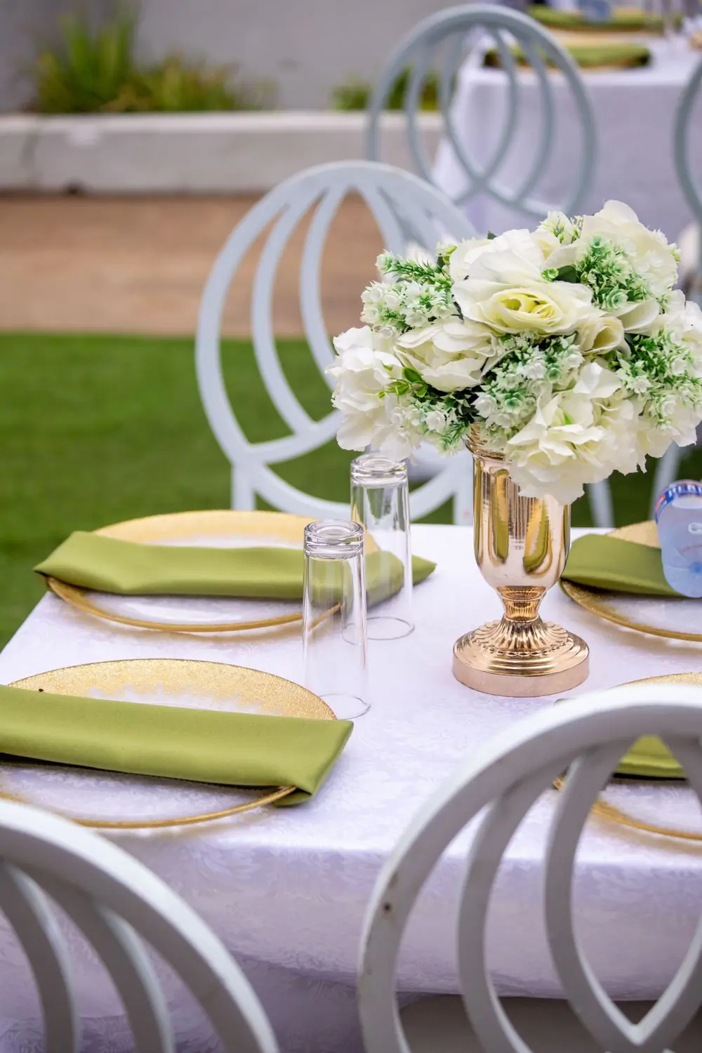 An outdoor table set with white flowers, gold chargers and sage napkins