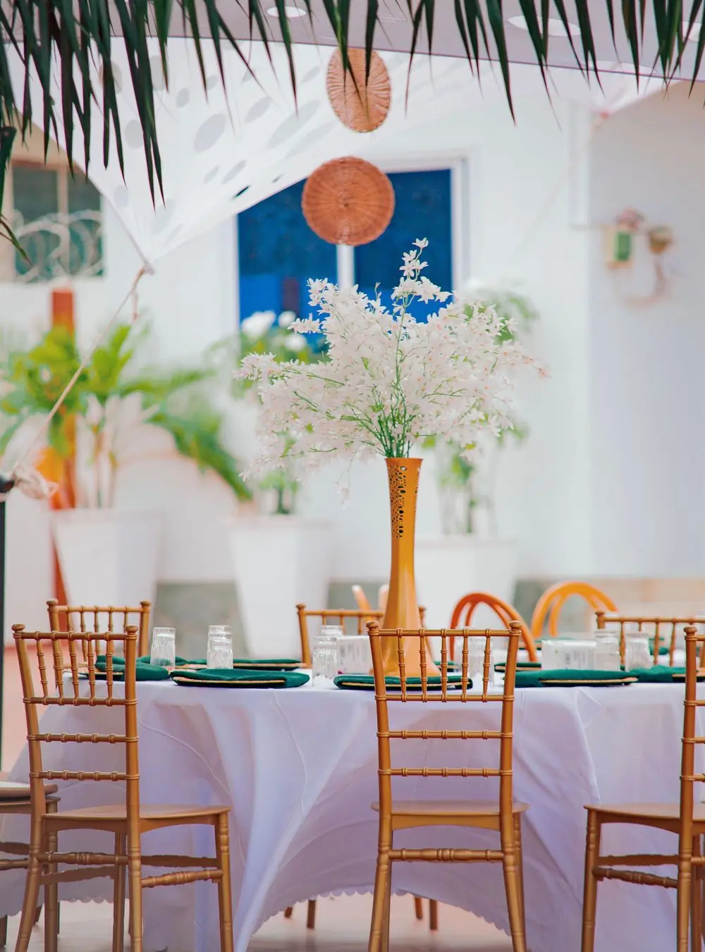 A garden table under palms with tall white blossom and rattan chairs