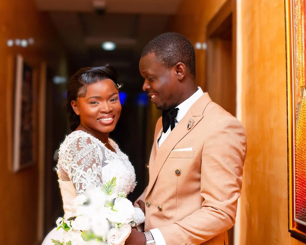 A newly married couple in a corridor, the groom in a peach suit