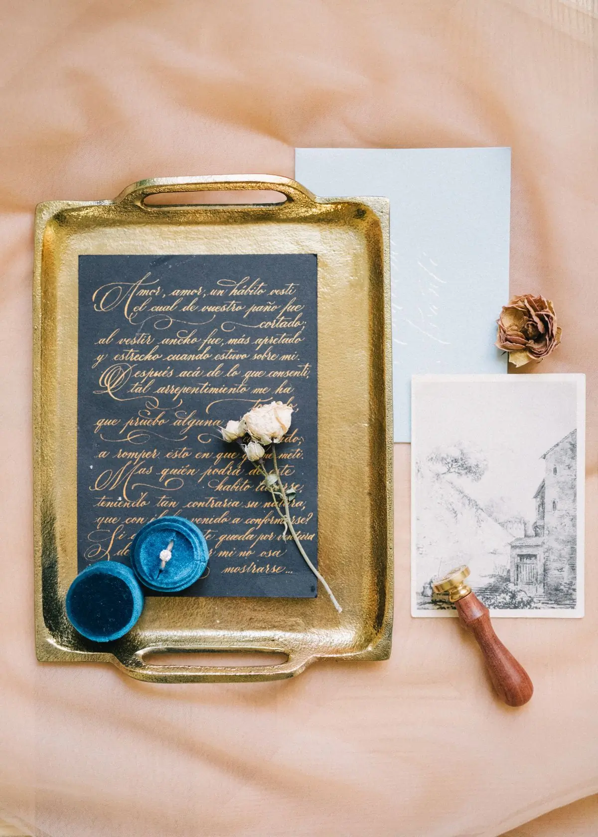 An invitation suite laid out on a gold tray with a wax seal and a dried rose