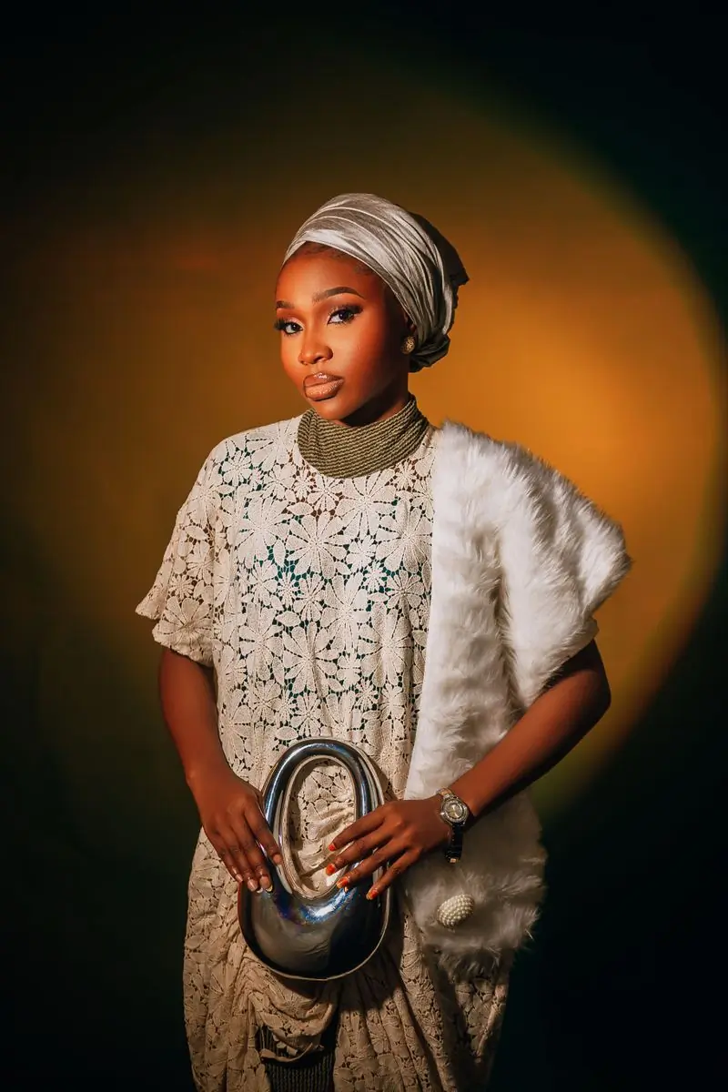A woman in an ivory brocade top and headwrap photographed under a warm light