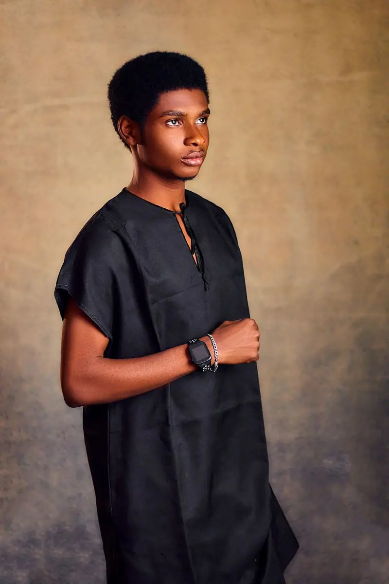 A young man in a plain dark tunic against an ochre backdrop