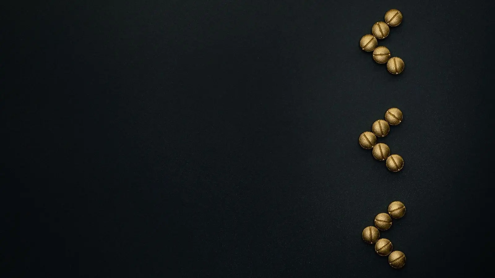 Gold capsules arranged in a column at the right of a deep black surface, open space to the left