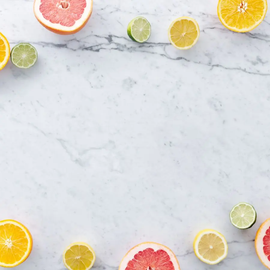 Halved oranges, limes, lemons and grapefruit framing the edges of a pale marble surface