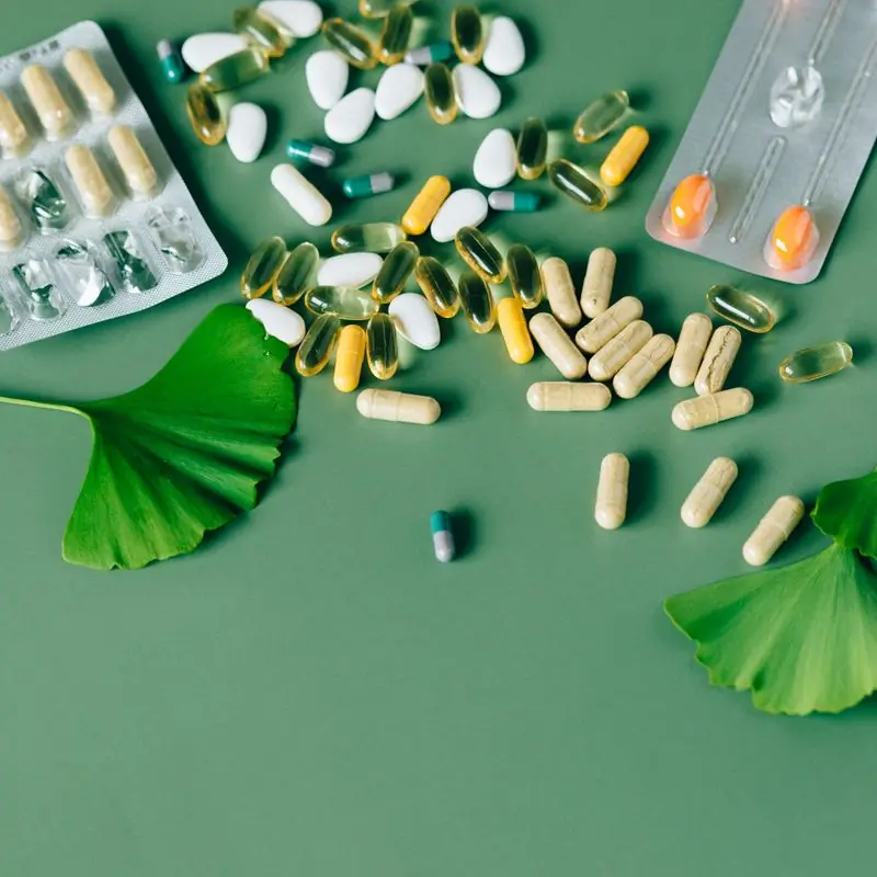 Capsules, tablets and blister packs spread on a green surface with ginkgo biloba leaves