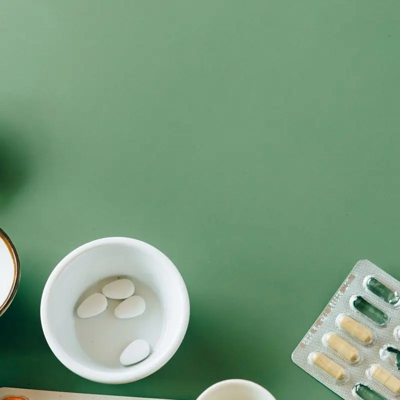 White bowls of supplements and a blister pack at the corners of a plain green field